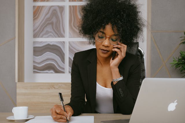 Person holding a phone to their ear while using a pen to write on paper